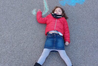 Petite fille allongée au sol sur lequel un parapluie est dessiné à la craie  - Agrandir l'image 3 sur 3, fenêtre modale