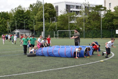 des enfants passant à travers un tunnel en plastique au sol, faisant la course  sur la pelouse du parc des sports des Maisons Rouges pour le Cross des Écoles 2024.  - Agrandir l'image 9 sur 9, fenêtre modale