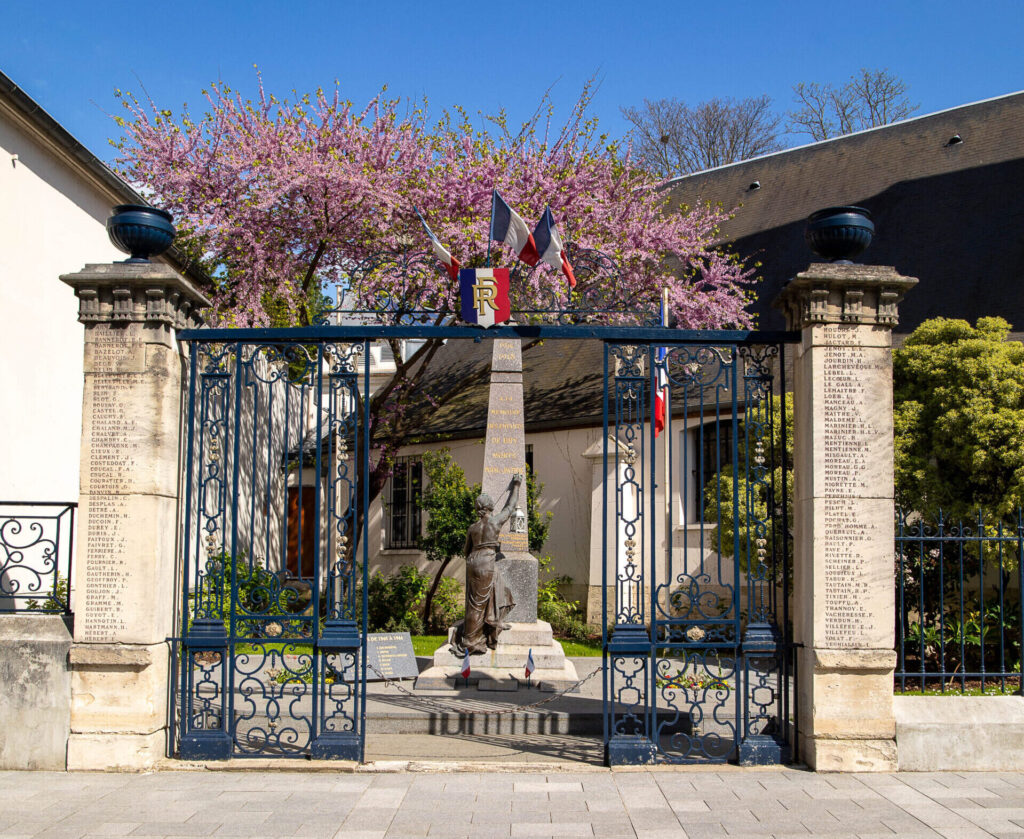 Portail donnant sur une petite place avec un monument au morts - Agrandir l'image, fenêtre modale