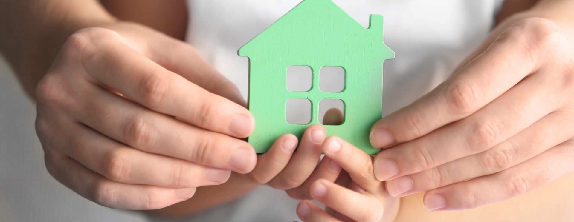 Maison verte tenue par la main d'un enfant et d'un adulte