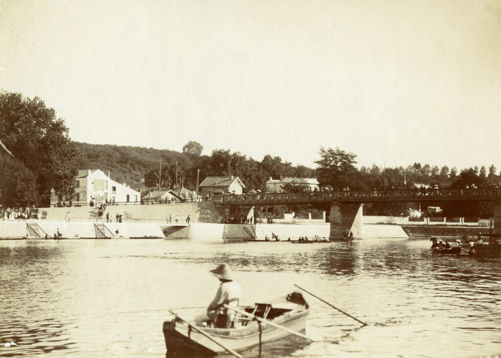 Photographie en noir et blanc. En premier plan, une personne sur une barque. En second plan, le pont qui traverse la Marne. - Agrandir l'image, fenêtre modale