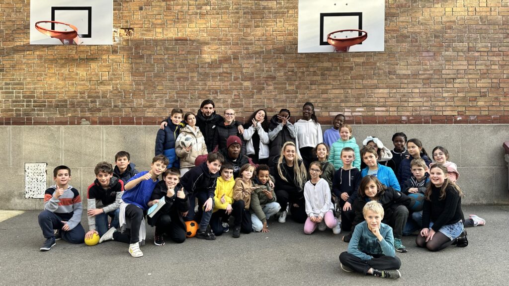 Enfants et jeunes assis devant un mur sur lequel est accroché un panier de basket - Agrandir l'image, fenêtre modale