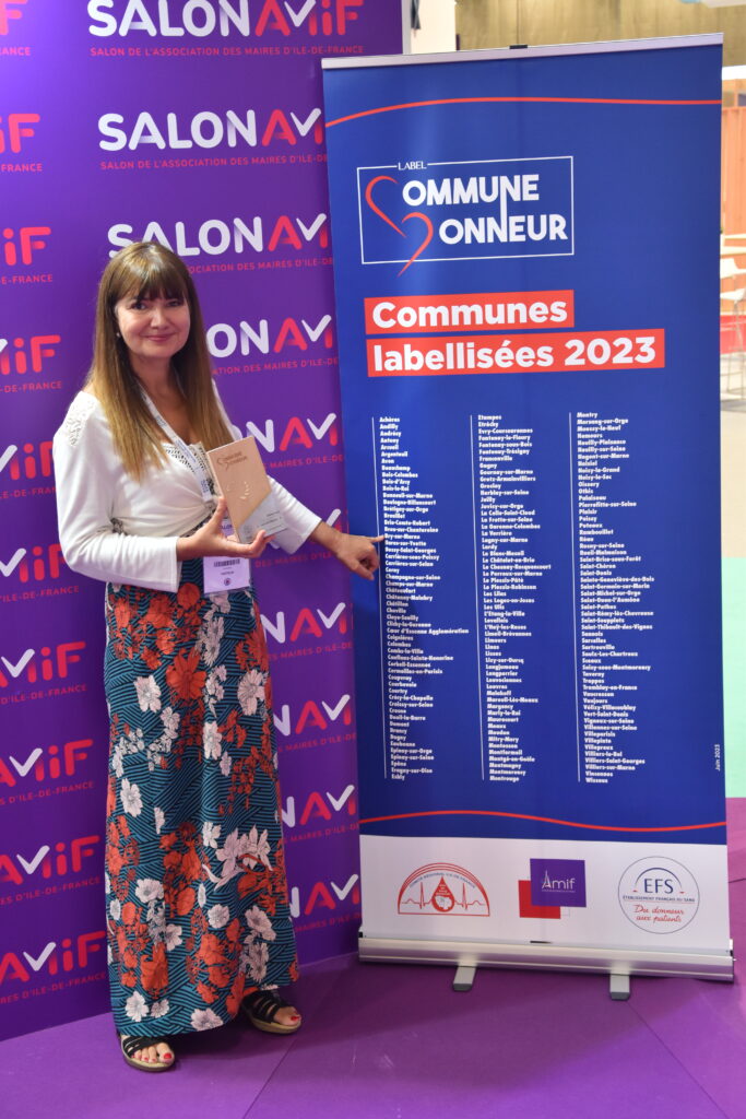 Femme devant un panneau qui recense des communes labellisées "Commune d'honneur"  - Agrandir l'image, fenêtre modale