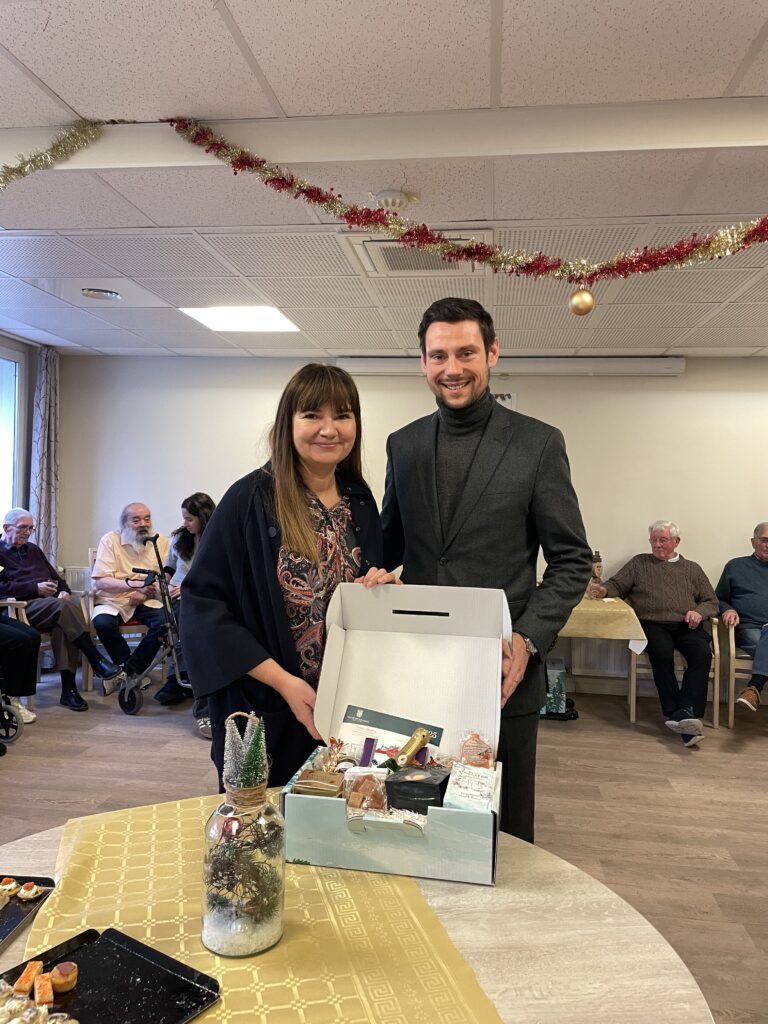 Monsieur le Maire et une membre du Conseil Municipal qui tiennent un colis destiné aux seniors dans les mains - Agrandir l'image, fenêtre modale