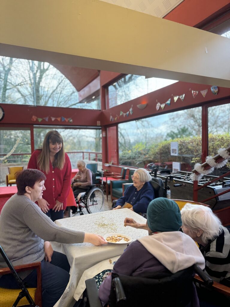 Membre du Conseil Municipal qui sourit à des personnes âgées assises autour d'une table - Agrandir l'image, fenêtre modale